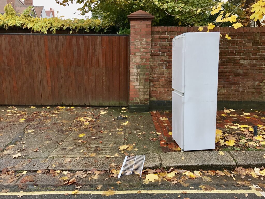 A white firdge standing outside on a pavement.