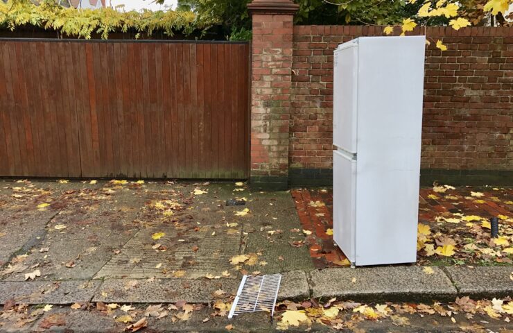 A white firdge standing outside on a pavement.